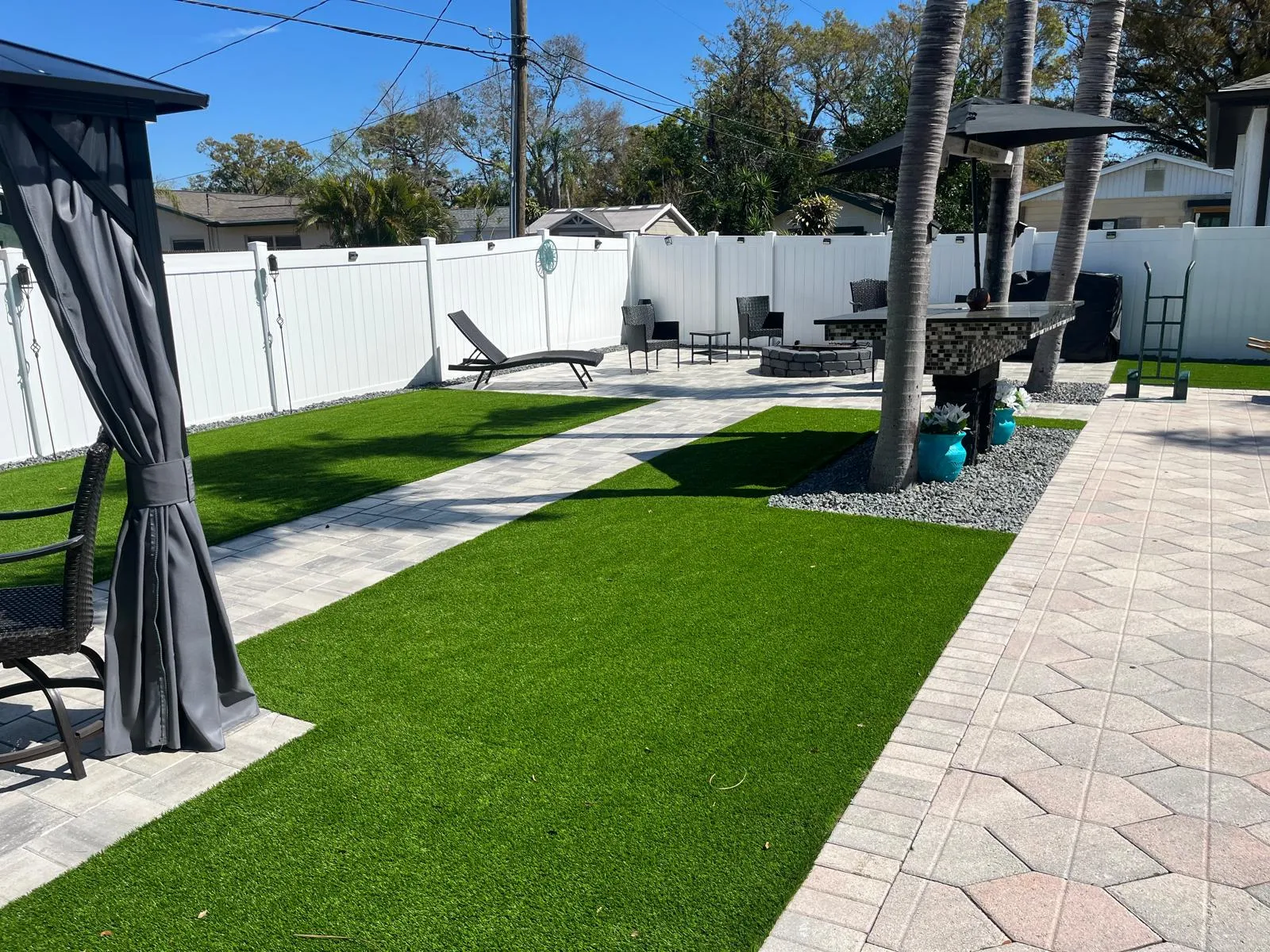 Backyard with artificial turf and paver walkways framed by palm trees
