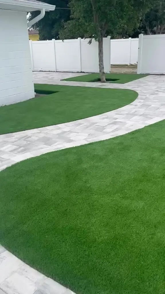 Curved gray paver path with artificial turf in a backyard